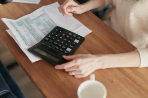 Mãos sobre uma mesa com um papel diagramado e uma calculadora, ilustrado a ideia de bitributação ao Simples Nacional.